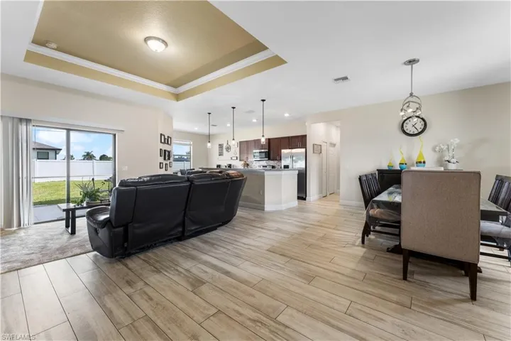 Living room with a tray ceiling, light wood-style floors, and visible vents