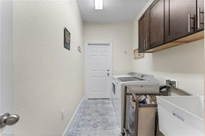 Laundry area featuring baseboards, a sink, a textured wall, cabinet space, and washer and clothes dryer