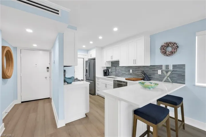Kitchen with backsplash, a kitchen bar, light wood finished floors, white cabinets, and light countertops