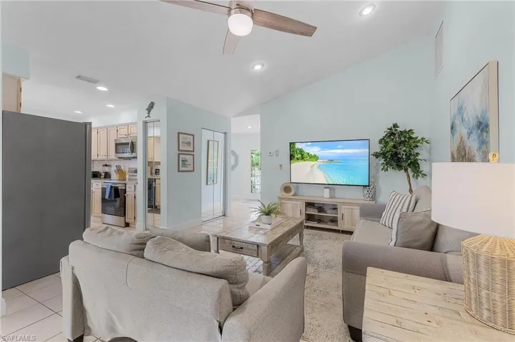 Living room with ceiling fan, light tile patterned floors, and vaulted ceiling