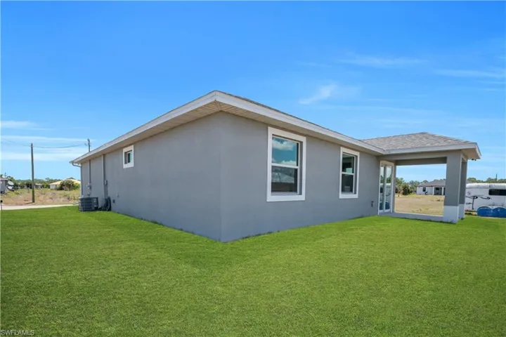 Expansive green lawn surrounds this stucco exterior home featuring a covered patio, multiple windows with white trim, and a shingled roof