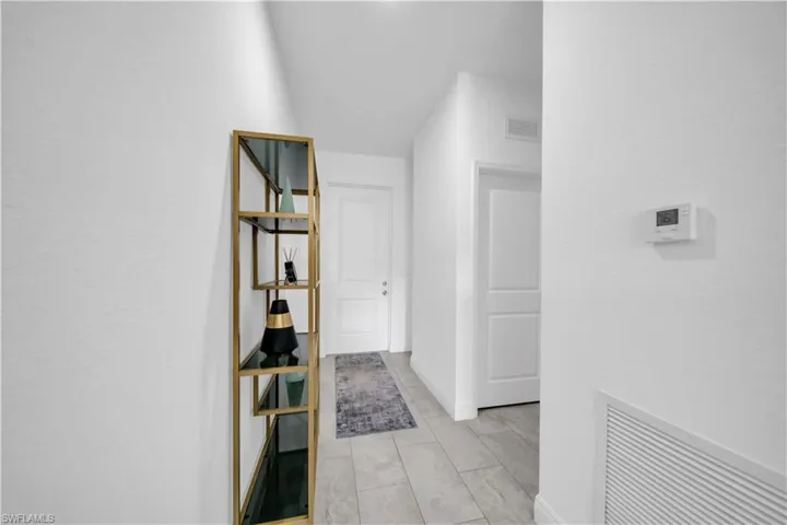 Hallway featuring light-toned tile flooring, white painted walls, and white interior doors with panel details