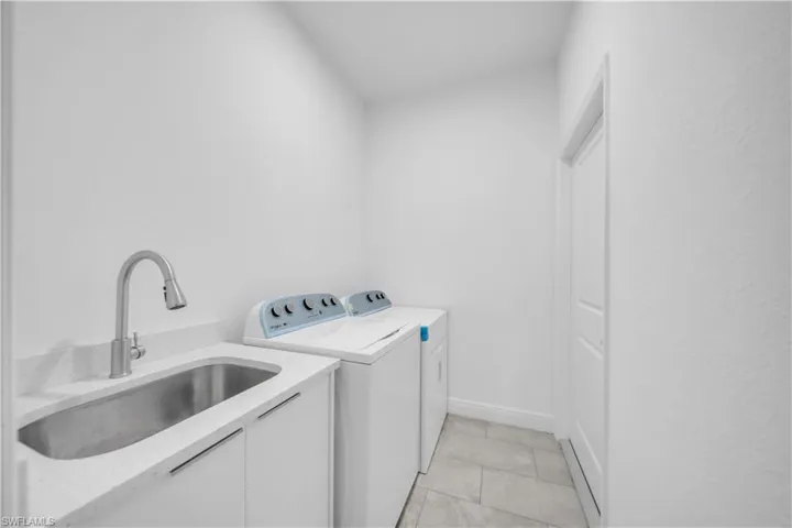 Laundry room featuring built-in cabinetry, an undermount sink with a gooseneck faucet, light-toned countertop, and tiled flooring