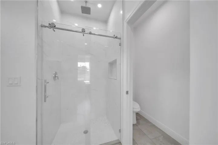 Modern shower enclosure with clear glass sliding door, polished chrome hardware, rainfall showerhead, and white hexagonal tile flooring