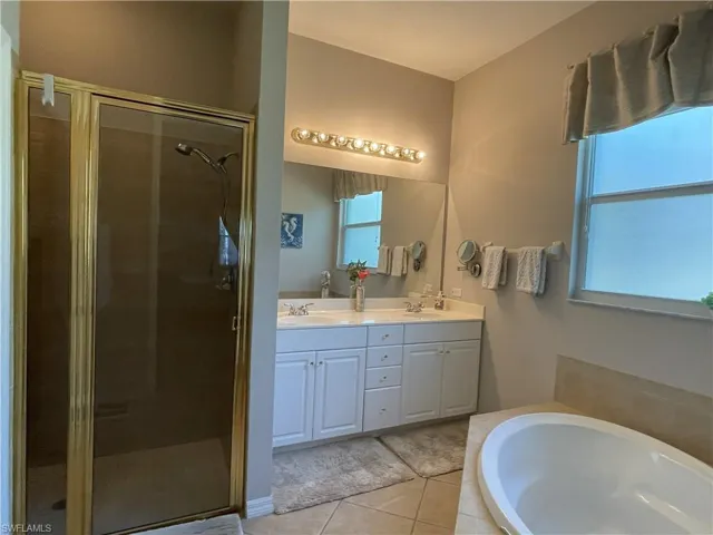 Master Bathroom with double vanity, a bath, light tile patterned floors, and a stall shower
