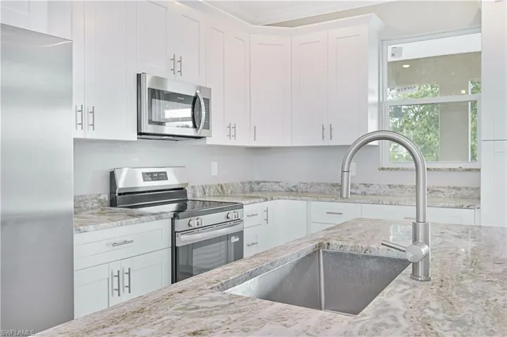 Kitchen with stainless steel appliances, white cabinets, light stone countertops, and crown molding