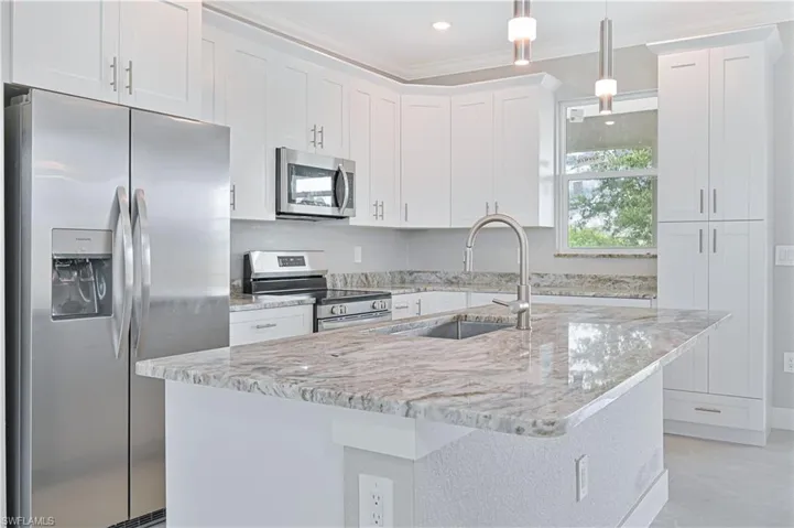 Kitchen with stainless steel appliances, ornamental molding, light stone countertops, white cabinetry, and a center island with sink
