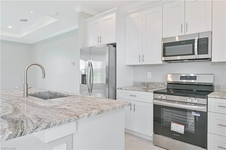 Kitchen with appliances with stainless steel finishes, white cabinets, crown molding, light stone countertops, and a raised ceiling