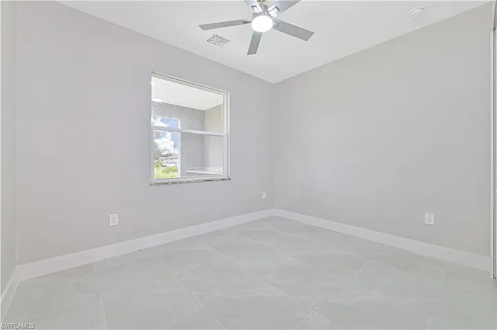 Empty room with a ceiling fan and light tile patterned flooring