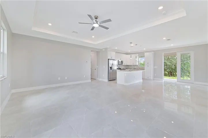 Unfurnished living room with a tray ceiling, ornamental molding, recessed lighting, and ceiling fan
