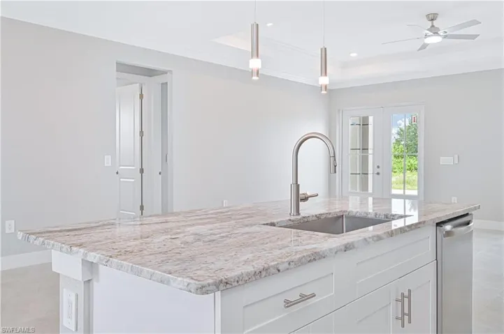 Kitchen with light stone countertops, white cabinets, ornamental molding, light tile patterned flooring, and pendant lighting