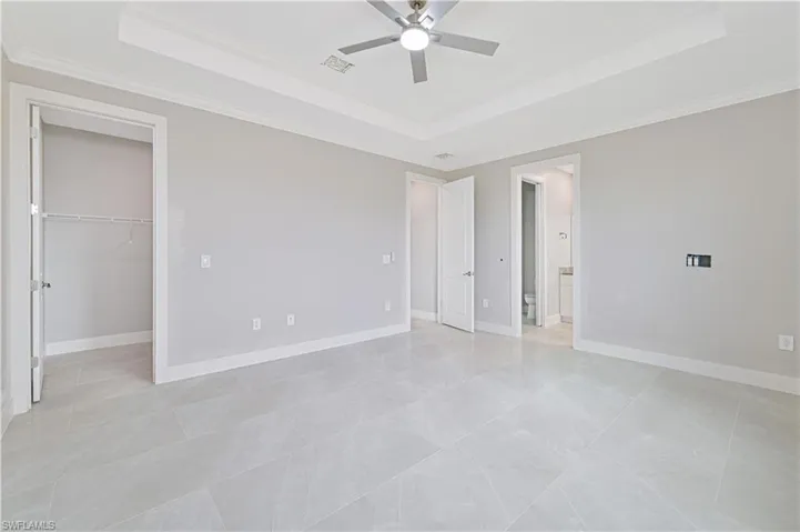 Unfurnished bedroom with a raised ceiling, crown molding, a walk in closet, and ceiling fan