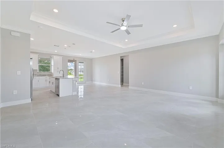 Spare room with a tray ceiling, ornamental molding, recessed lighting, ceiling fan, and light marble finish floors