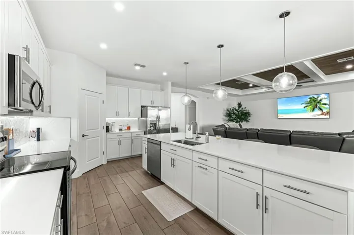 Kitchen featuring appliances with stainless steel finishes, white cabinetry, decorative light fixtures, backsplash, and recessed lighting