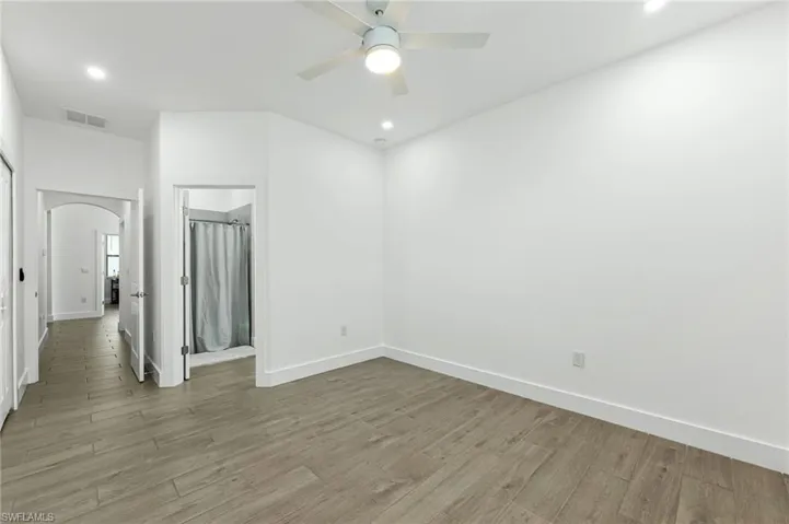Empty room featuring light wood-style floors, arched walkways, recessed lighting, and a ceiling fan