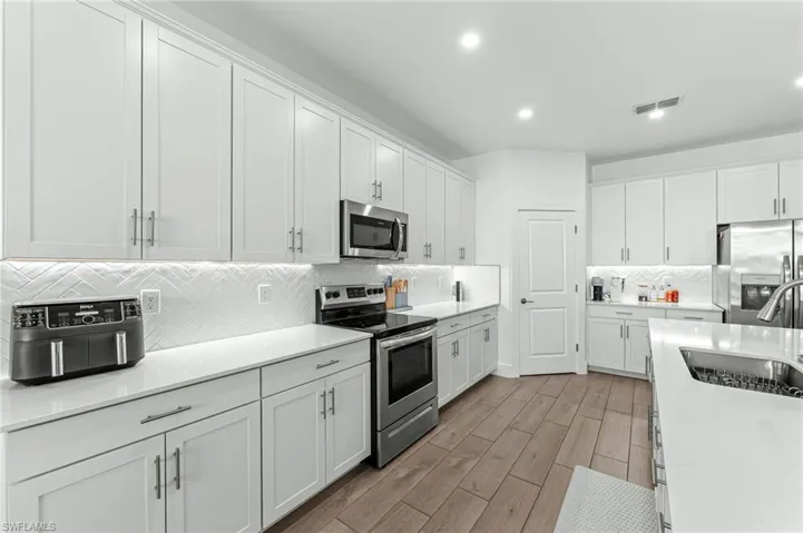 Kitchen with white cabinets, appliances with stainless steel finishes, tasteful backsplash, wood finish floors, and recessed lighting