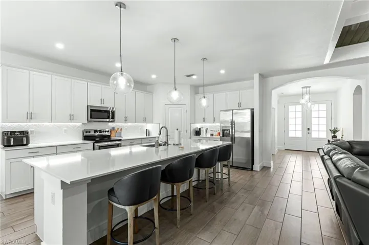 Kitchen with arched walkways, stainless steel appliances, white cabinetry, a kitchen breakfast bar, and a large island