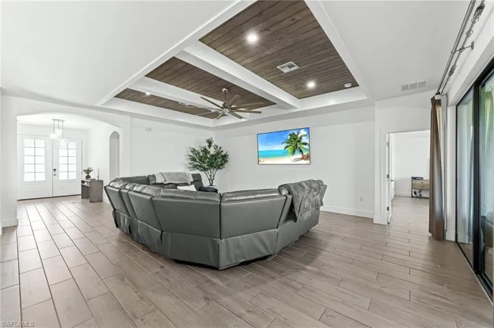 Living room featuring a wooden ceiling with exposed beams, wood tiled floors, a ceiling fan, arched walkways, and french doors