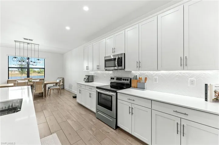 Kitchen featuring appliances with stainless steel finishes, white cabinetry, tasteful backsplash, hanging light fixtures, and recessed lighting