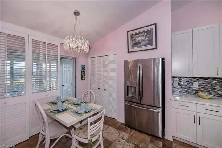 Kitchen with stainless steel refrigerator with ice dispenser, vaulted ceiling, a notable chandelier, tasteful backsplash, and dark tile flooring