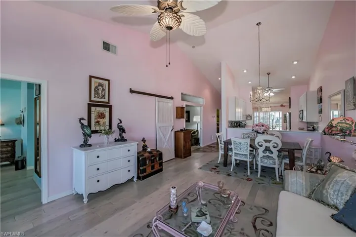 Living room featuring a barn door, high vaulted ceiling, light hardwood / wood-style flooring, and ceiling fan with notable chandelier