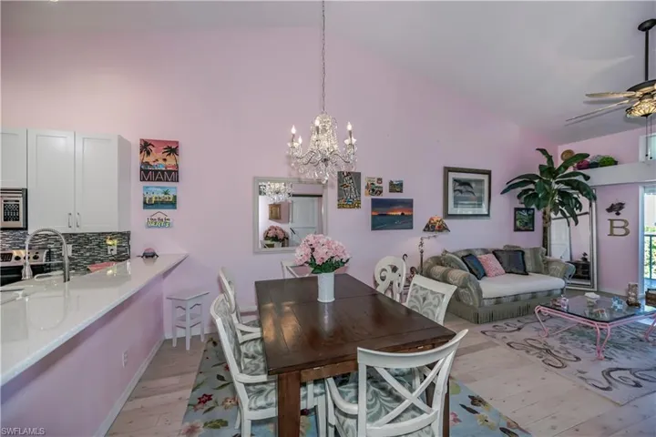 Dining space featuring high vaulted ceiling, sink, ceiling fan with notable chandelier, and light hardwood / wood-style flooring