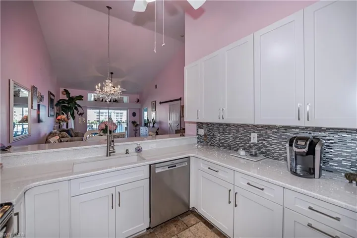 Kitchen with white cabinetry, ceiling fan with notable chandelier, stainless steel dishwasher, sink, and light tile floors