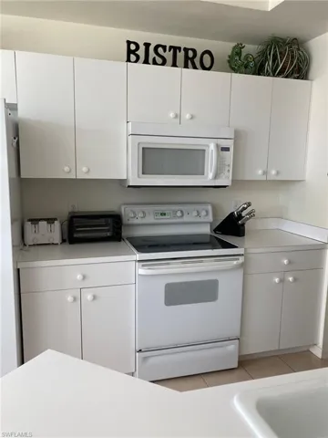 Kitchen featuring white appliances, white cabinets, light countertops, and light tile patterned floors