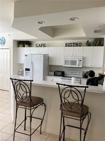 Kitchen with white appliances, a tray ceiling, light tile patterned floors, a breakfast bar area, and white cabinets