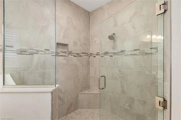 Glass-enclosed shower featuring large format wall tiles, a decorative mosaic tile band, a built-in shower niche, a corner bench, and a rainfall showerhead