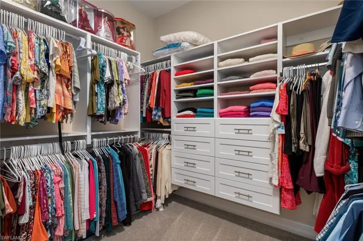 Custom-built walk-in Primary closet featuring extensive hanging storage, multiple open shelving units, integrated drawer storage with brushed nickel hardware, and neutral carpet flooring