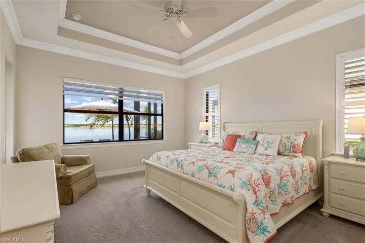 Window with water frontage, tray ceiling with crown molding, ceiling fan, carpet flooring, and plantation shutters