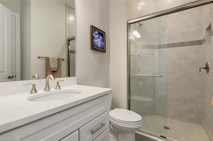 Bathroom featuring a white vanity with an undermount sink, brushed nickel fixtures, a frameless shower enclosure, a tiled shower surround, and a built-in shower niche