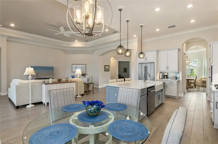 Open-concept living space featuring a central kitchen island with seating, pendant lighting, wood-finish flooring, recessed lighting, and crown molding