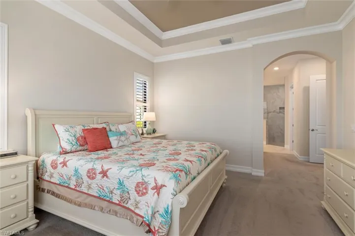 Bedroom featuring tray ceiling with crown molding, plantation shutters, and soft carpet flooring