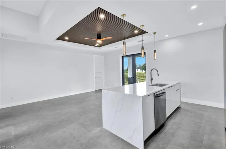 Kitchen featuring sink, decorative light fixtures, a raised ceiling, a kitchen island with sink, and dishwasher