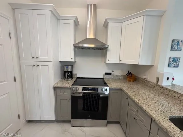 Kitchen featuring stainless steel range with electric cooktop, light stone counters, light marble finish floors, and two tone cabinetry