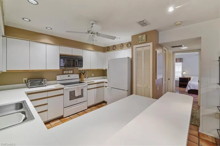 Kitchen with white cabinets, light countertops, white appliances, a ceiling fan, and light tile patterned floors