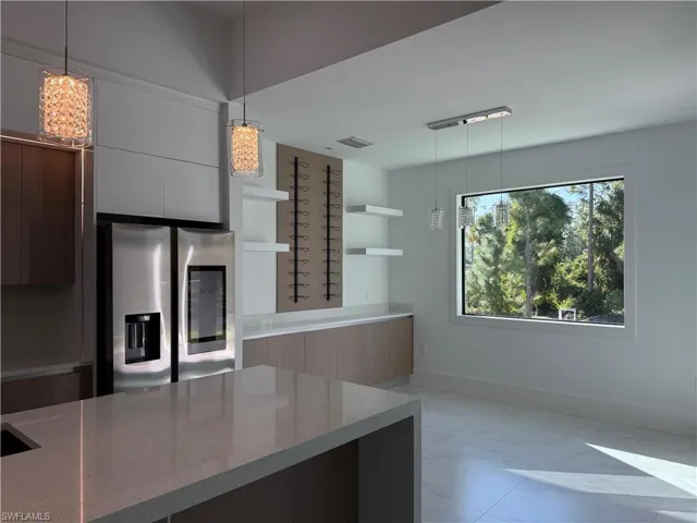 Kitchen with modern cabinets, decorative light fixtures, open shelves, stainless steel refrigerator with ice dispenser, and light stone countertops