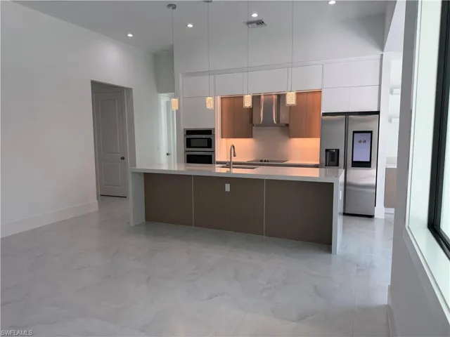 Kitchen featuring modern cabinets, appliances with stainless steel finishes, pendant lighting, a spacious island, and light stone countertops