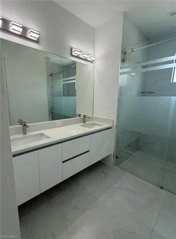 Bathroom with a marble finish shower, double vanity, and light marble finish flooring