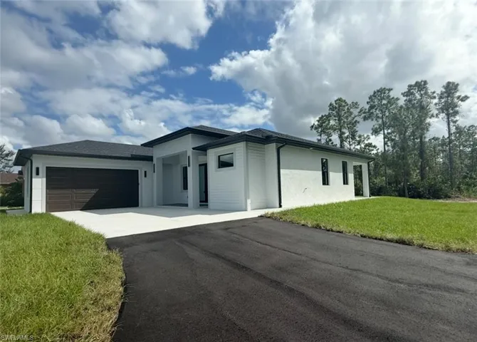 View of front of house featuring a front yard, driveway, a garage, and stucco siding
