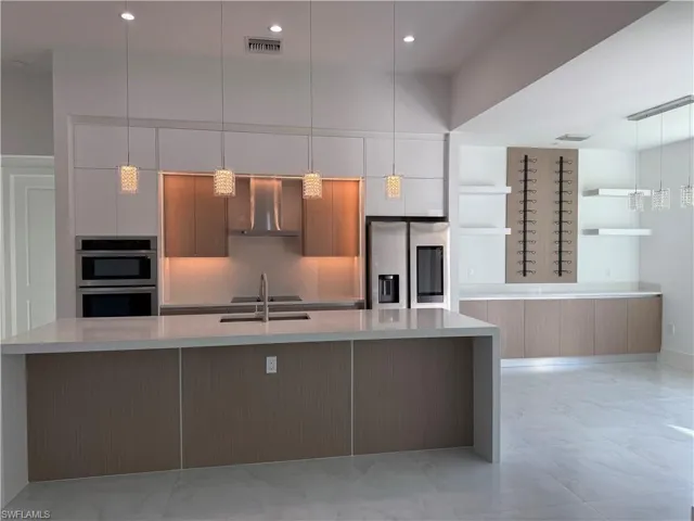 Kitchen with modern cabinets, light stone counters, open shelves, decorative light fixtures, and appliances with stainless steel finishes