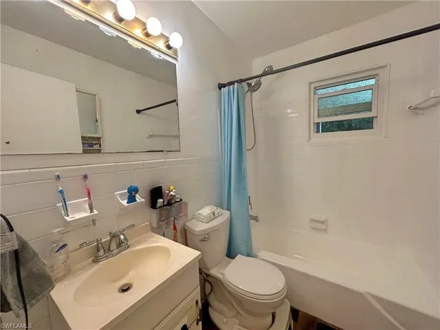 Full bathroom with backsplash, toilet, vanity, shower / tub combo with curtain, and tile walls