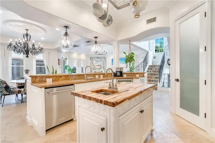 Kitchen featuring white cabinetry, stainless steel dishwasher, decorative light fixtures, ornamental molding, and open floor plan