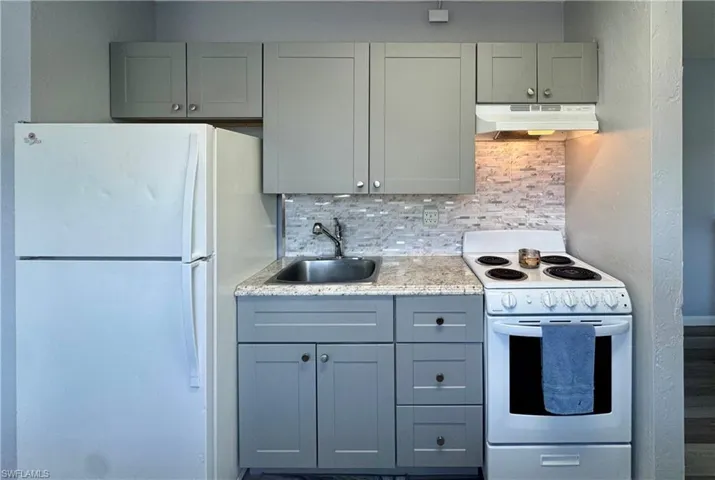Kitchen featuring white appliances, decorative backsplash, gray cabinets, and under cabinet range hood