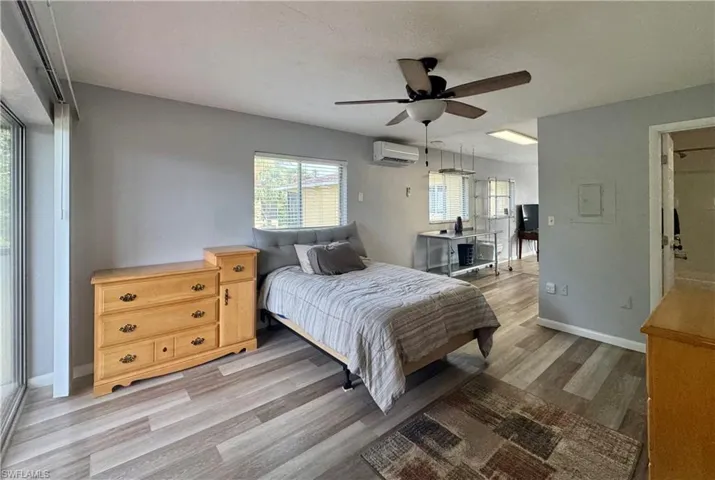 Bedroom with light wood-type flooring, a ceiling fan, and a wall unit AC