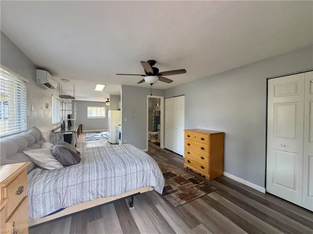 Bedroom featuring dark wood-type flooring, an AC wall unit, two closets, ceiling fan, and freestanding refrigerator