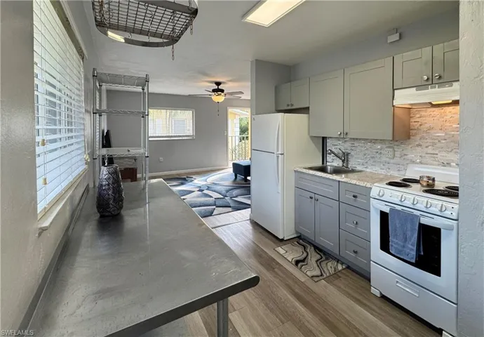 Kitchen featuring white appliances, under cabinet range hood, light wood-type flooring, tasteful backsplash, and gray cabinets