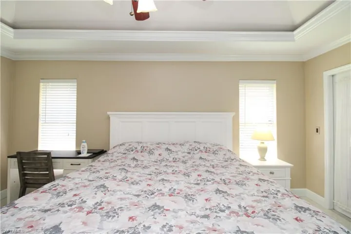 Bedroom featuring ceiling fan, baseboards, multiple windows, and ornamental molding